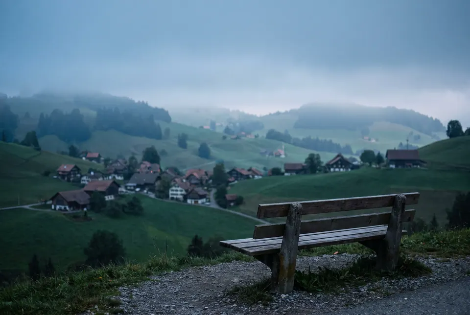 Leere Holzbank auf einem Kiesweg mit Blick über grüne Hügel