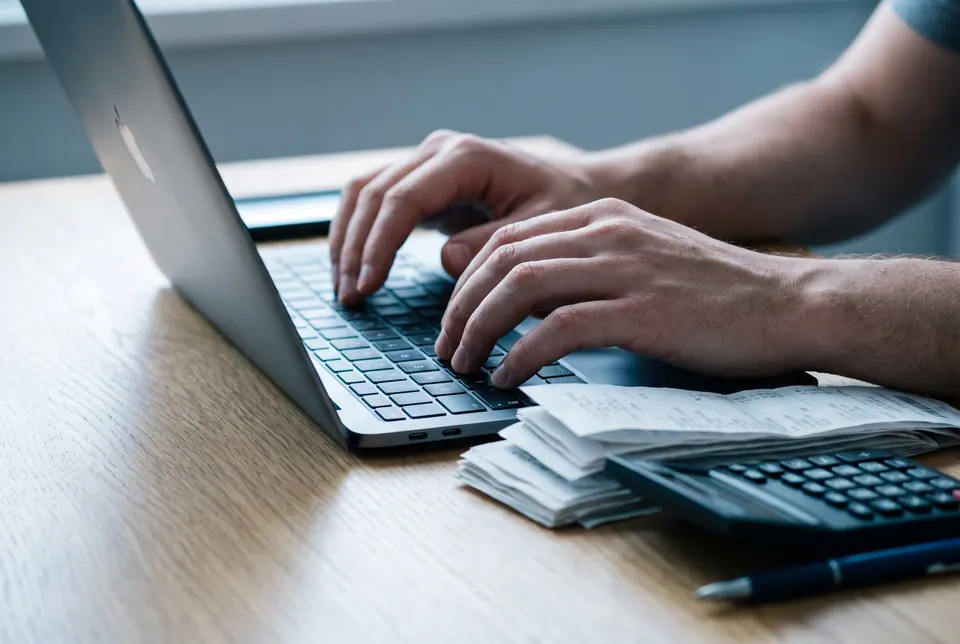 Hände tippen auf einem Laptop neben Belegen