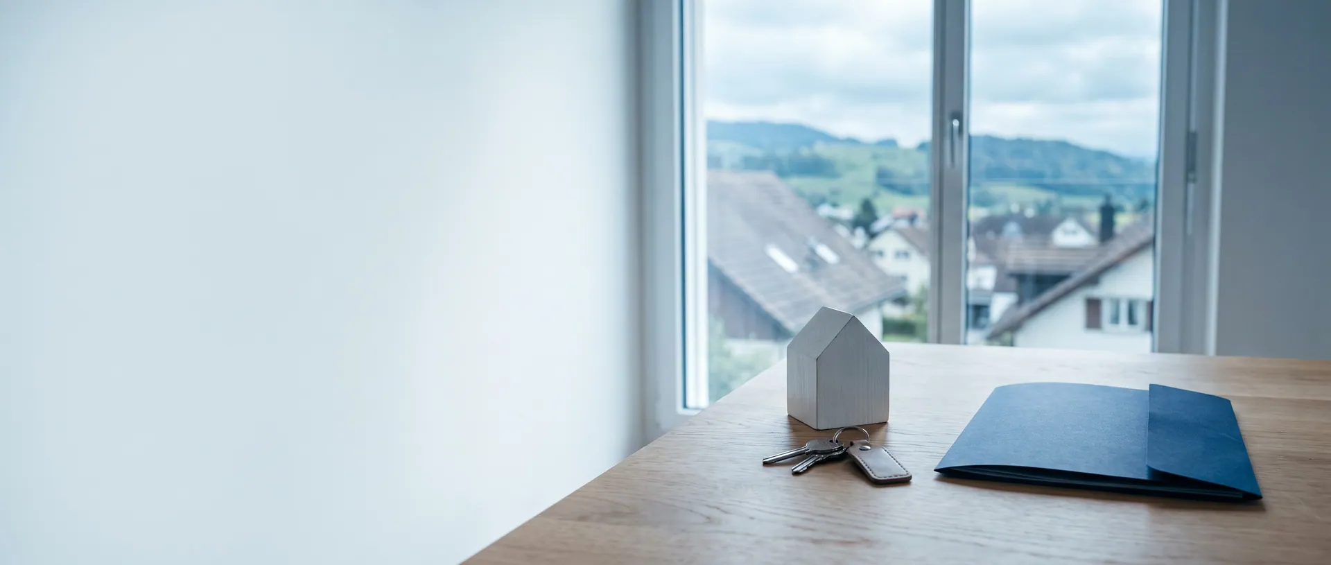 Hausmodell und Schlüssel auf einem Holztisch vor dem Fenster