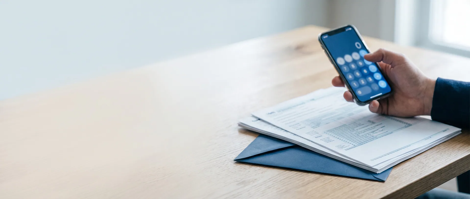 Hand mit Smartphone über Steuerunterlagen